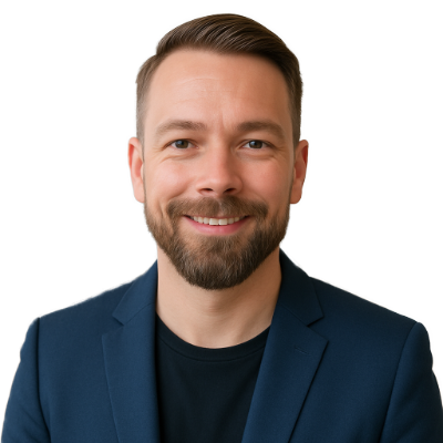 Ein lächelnder Mann mit kurzen braunen Haaren und einem Bart, der einen dunklen Blazer über einem schwarzen Hemd trägt, posiert vor einem schlichten weißen Hintergrund, bereit, Hausmeisterservice und zuverlässige Grünflächenpflege zu bieten.