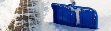 Eine blaue Schneeschaufel liegt in einem Schneehaufen neben einem geräumten Ziegelweg und zeugt vom jüngsten Schaufeln - einer der vielen Hausmeisterdienste, die neben Reperaturen und Grünflächenpflege angeboten werden.